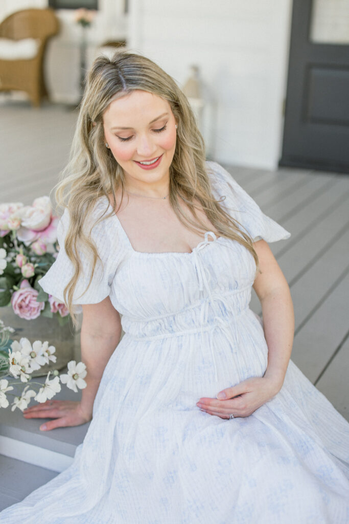 Mom holding her growing belly on a porch in the spring during a motherhood portrait mini in Tomball Texas . 