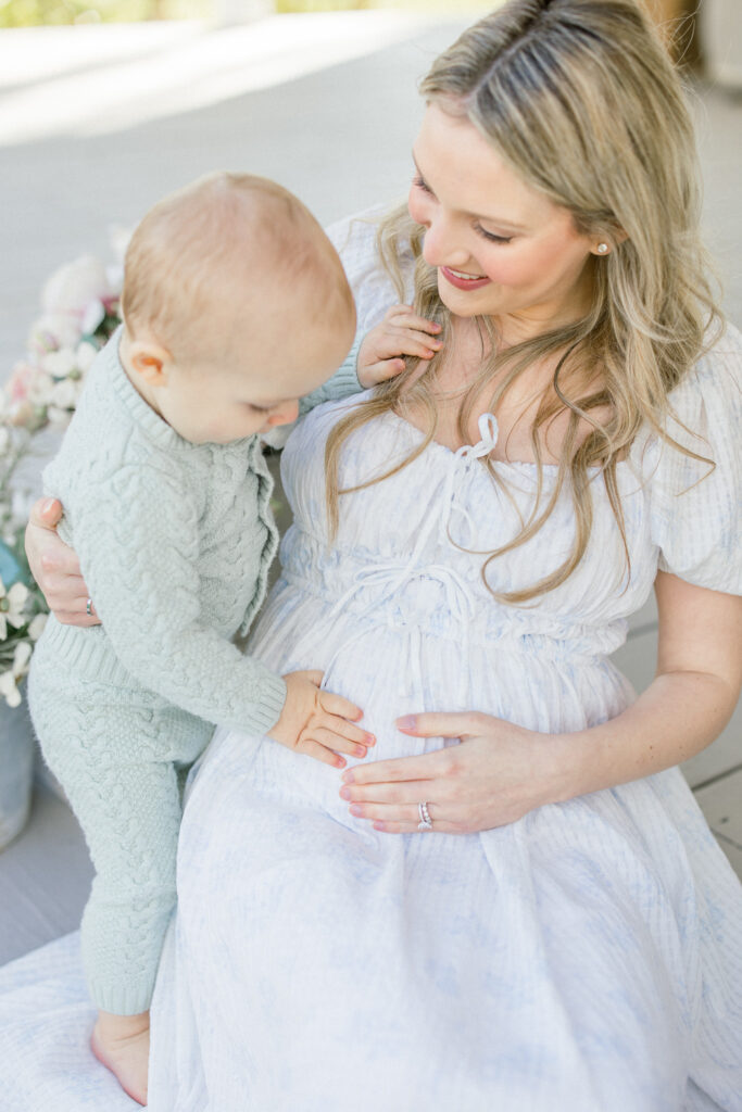 toddler touching moms belly to see where baby sister is on a front porch in Tomball during a motherhood portrait session
