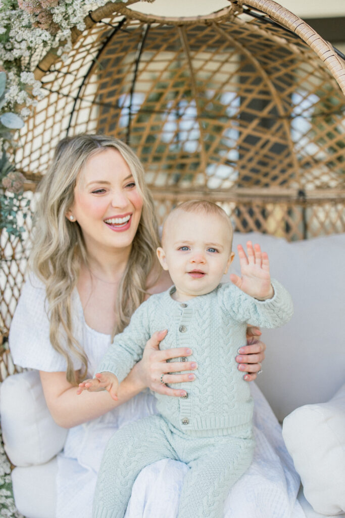 Toddler son waving hi to photographer during spring time session on a front porch in Tomball 